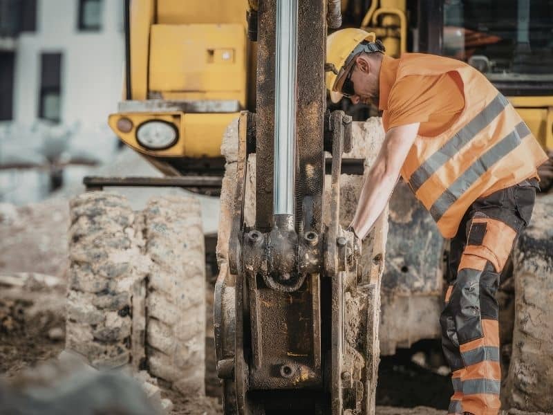Construction worker operating muddy equipment while construction resumes after severe weather disruptions